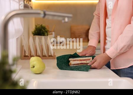 Uomo che confeziona il sandwich in una confezione di cibo in cera d'api sul ripiano bianco della cucina, primo piano Foto Stock