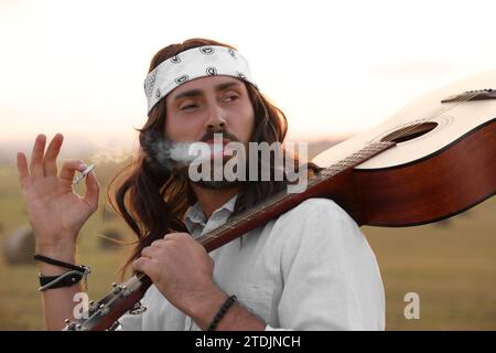 Elegante uomo hippie con fumante chitarra in campo Foto Stock