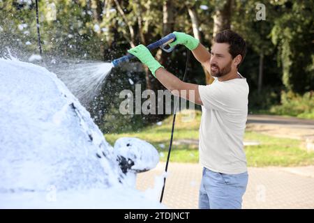 Uomo che copre l'automobile con schiuma all'autolavaggio esterno Foto Stock