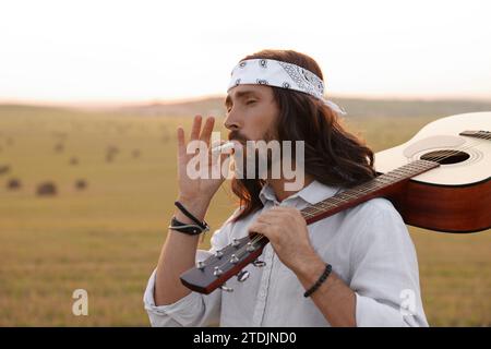 Elegante uomo hippie con fumante chitarra sul campo, spazio per il testo Foto Stock