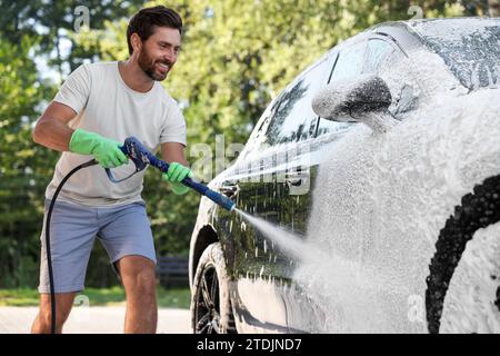 Uomo che copre l'automobile con schiuma all'autolavaggio esterno Foto Stock