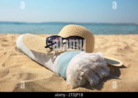 Cappello di paglia, asciugamano e occhiali da sole sulla spiaggia sabbiosa Foto Stock