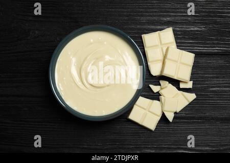 Gustosa pasta di cioccolato bianco in ciotola e pezzi su un tavolo di legno nero, vista dall'alto Foto Stock