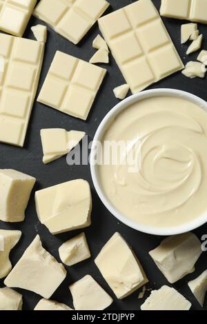 Gustosa pasta di cioccolato bianco in ciotola e pezzi su tavolo nero, piatto Foto Stock