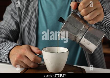 Uomo che versa il caffè aromatico della moka in una tazza al tavolo bianco, primo piano Foto Stock