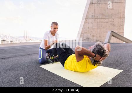 allenatore che aiuta l'uomo sportivo senior con l'allenamento abs Foto Stock
