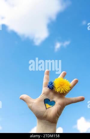 mano dei bambini con un cuore giallo e blu disegnato sul palmo contro il cielo Foto Stock