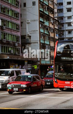 Un taxi e un autobus di Hong Kong - tra le altre auto - aspettano al semaforo in un trafficato incrocio di Hong Kong. Foto Stock