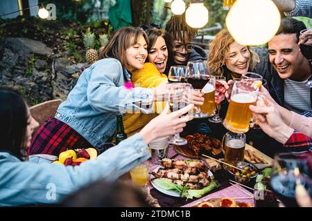 Allegro gruppo di diversi amici che brindano con vino e birra, che si godono una festa barbecue all'aperto, condividendo risate e felicità Foto Stock