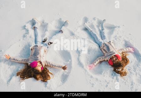 Due ragazze su un angelo di neve spettacoli. Bambini sorridenti sdraiati sulla neve con spazio fotocopie. Bambini che giocano e fanno un angelo di neve nella neve. Vista dall'alto. Foto Stock