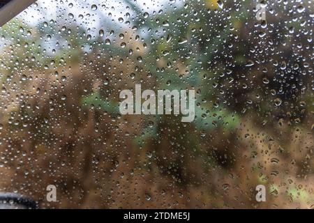 gocce di pioggia che scivolano sul vetro del finestrino dell'auto durante le giornate piovose da un angolo piatto Foto Stock