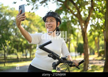 Donna di mezza età seduta su una bicicletta e che effettua una videochiamata sul cellulare Foto Stock