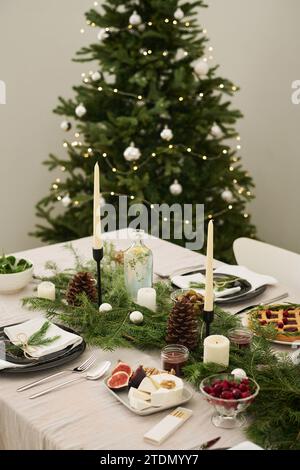 Tavolo natalizio decorato con candele e rami di abete con albero di natale sullo sfondo Foto Stock