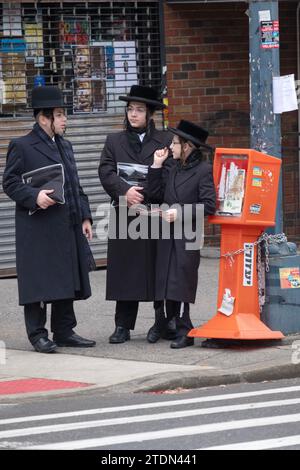 3 ragazzi ebrei ortodossi, probabilmente in viaggio dai servizi del tempio, hanno una conversazione informale all'angolo della strada a Brooklyn, New York. Foto Stock