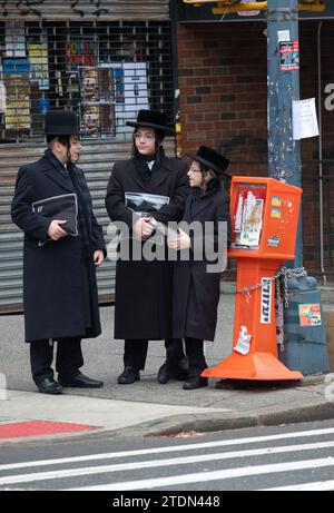 3 ragazzi ebrei ortodossi, probabilmente in viaggio dai servizi del tempio, hanno una conversazione informale all'angolo della strada a Brooklyn, New York. Foto Stock