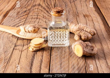Olio di radice di zenzero naturale fatto in casa in bottiglia con tappo in sughero su fondo di legno tra le radici di zenzero. Cura di sé a casa. Foto Stock