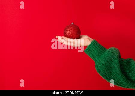 Donne con un maglione verde che regge il simbolo del nuovo anno nelle sue mani: Una pallina di Natale rossa. Foto Stock