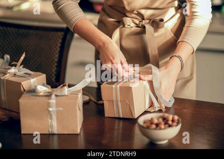 Primo piano le mani delle donne legano il nastro sulla scatola per l'ordine del cliente. Pasticceria e torta in cucina. Imprenditore di piccole imprese e cibo Foto Stock