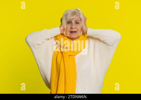 Non voglio sentire e ascoltare. Frustrata infastidita irritata anziana che copre le orecchie gestando senza evitare consigli ignorando il rumore sgradevole le voci rumorose. Nonna isolata su sfondo giallo Foto Stock