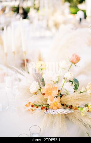 Bouquet di fiori si trova su un tavolo festivo vicino a bicchieri vuoti Foto Stock