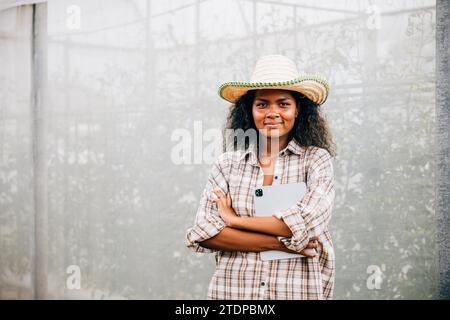 PhotoSuccessful proprietario di una serra una giovane donna con una camicia a quadri e grembiule in piedi con le braccia incrociate Foto Stock