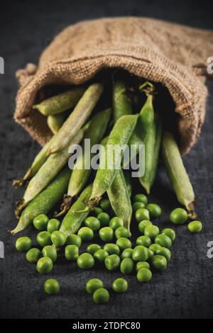 piselli sbucciati verdi in un recipiente su sfondo nero Foto Stock