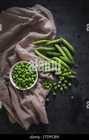 piselli sbucciati verdi in un recipiente su sfondo nero Foto Stock