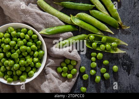 piselli sbucciati verdi in un recipiente su sfondo nero Foto Stock