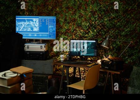 Foto in basso del luogo di lavoro di un ufficiale militare con lampada da tavolo e due schermi di computer con informazioni provenienti dalle telecamere Foto Stock