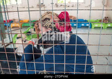 Giovane ragazza che accarezza il cane randagio in gabbia nel rifugio per animali domestici. Persone, animali, volontariato e concetto di aiuto. Foto Stock