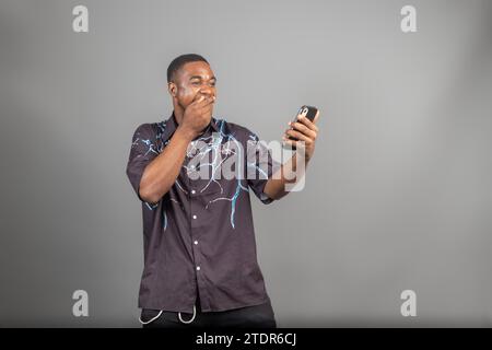 Allegro uomo nero Millennial casual che usa uno smartphone moderno, controlla i social media e guarda lo spazio di copia per le applicazioni mobili Foto Stock