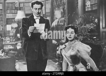 Michael Wilding e Paulette Goddard recitano in "An Ideal Husband" (1947), un adattamento cinematografico del dramma classico di Oscar Wilde. Wilding interpreta il suave ma tormentato Sir Robert Chiltern, il cui passato minaccia il suo presente, mentre Goddard interpreta l'astuta e affascinante signora Cheveley, che detiene un segreto che potrebbe rovinare la carriera di Chiltern. Le loro esibizioni, traboccanti di eleganza e spirito, danno vita alla versione satirica di Wilde sull'alta società vittoriana. Foto Stock