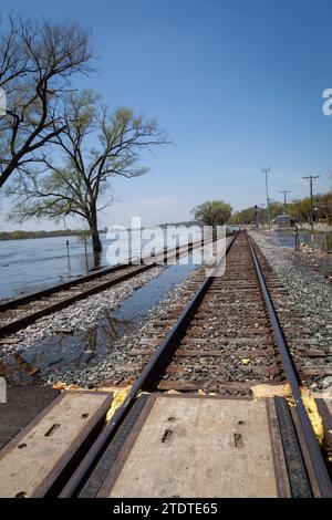 I binari ferroviari stanno per essere superati da un fiume allagato. Foto Stock