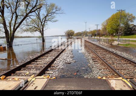 I binari ferroviari stanno per essere superati da un fiume allagato. Foto Stock