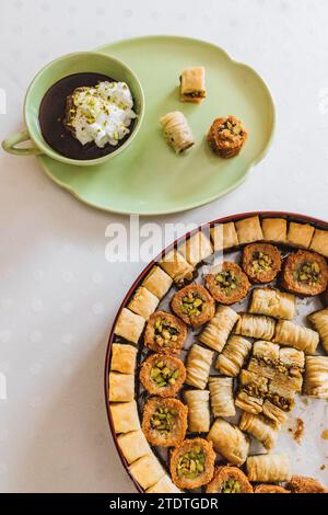 cioccolata calda da bere in tazza verde abbinata e piatto con dessert assortiti di baklava su tovaglia a pois bianca Foto Stock