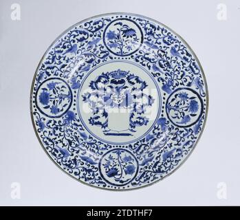 Piatto con stemma vuoto, piante fiorite e rotoli, anonimo, c. 1675 - c. 1699 piattino in porcellana, dipinto in blu sotto smalto. Sull'appartamento in un doppio medaglione, uno stemma vuoto con una corona e viti a foglia come elmetto. Sul muro e sul bordo vigne foglie con uccelli interrotti da quattro medaglioni con piante fiorite. Sotto due medaglioni due volte una figura umana che tiene il ramo del fiore sopra la sua testa. Il piatto è stato rotto; sedici prenes sul fondo. Performance europea in Blauw-WIT. Porcellana giapponese. glassa. Pittura cobalto (minerale) / porcellana vetrificazione Foto Stock