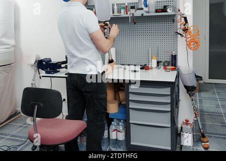 Ritagliare un artigiano irriconoscibile che regola e piega la gamba protesica moderna nella sezione del ginocchio Foto Stock