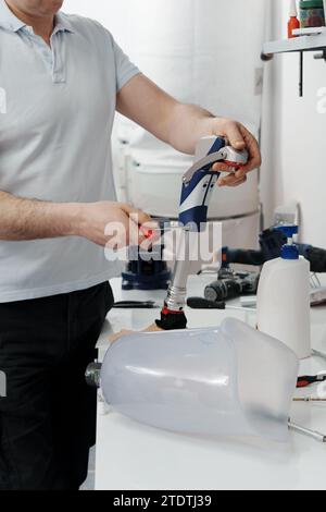 Ritagliare un artigiano irriconoscibile che regola e piega la gamba protesica moderna nella sezione del ginocchio Foto Stock