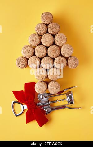 Tappi di champagne disposti a forma di albero di Natale e un cavatappi di metallo legato con un nastro su sfondo giallo Foto Stock