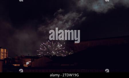 I fuochi d'artificio illuminano e illuminano un cielo nero sul tetto di alcune case Foto Stock