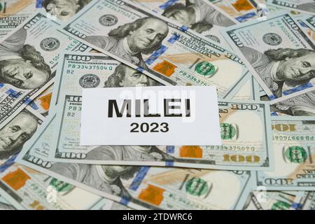 Carta di piccole dimensioni con la parola "Milei 2023" su sfondo con centinaia di bollette da dollari. Focus sulla parola "Milei" Foto Stock