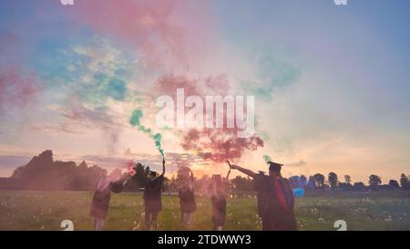 Gli studenti si laureano con fumo colorato che cammina attraverso il prato la sera. Foto Stock