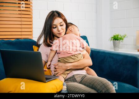 Una madre lavora in modo efficiente dal suo ufficio domestico digitando sul suo laptop mentre sua figlia dorme Foto Stock