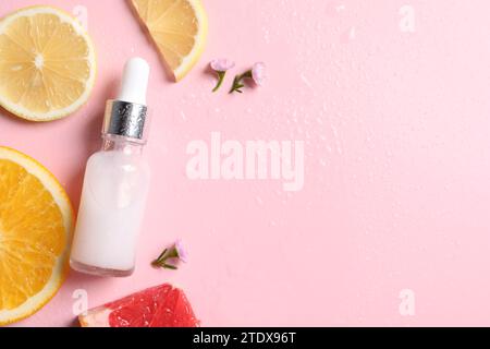 Bottiglia di siero cosmetico, agrumi a fette e fiori piccoli su sfondo rosa bagnato, piatto. Spazio per il testo Foto Stock