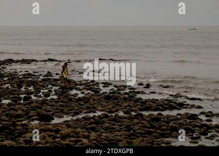 Contemplazione costiera: Un abitante locale si ferma in mezzo al paesaggio roccioso, trovando conforto nell'intramontabile convergenza tra mare e pietra. Foto Stock