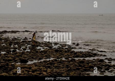 Contemplazione costiera: Un abitante locale si ferma in mezzo al paesaggio roccioso, trovando conforto nell'intramontabile convergenza tra mare e pietra. Foto Stock