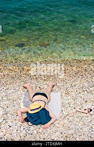 Torri del Benaco: Donna sdraiata a faccia in giù sulla spiaggia, cappello da sole, bikini, Lago di Garda a Verona, Veneto, Italia Foto Stock