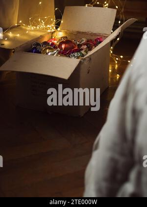 Immagine verticale di una scatola aperta con decorazioni vintage sull'albero di Natale e moderne luci elettriche in una camera da letto. Foto Stock