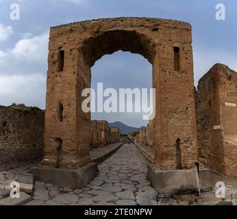 Pompei, Italia - 25 novembre 2023: Arco in pietra e lunga strada nell'antica città di Pompei Foto Stock