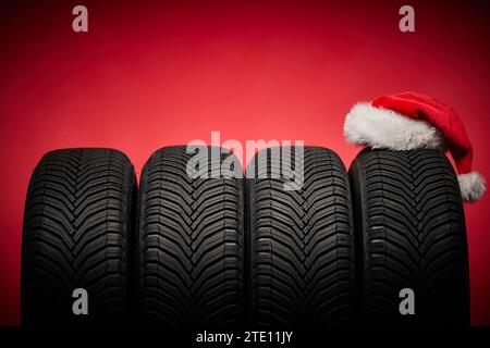 Pneumatici invernali, ruote grandi e cappello di Babbo Natale sfondo rosso natalizio Foto Stock